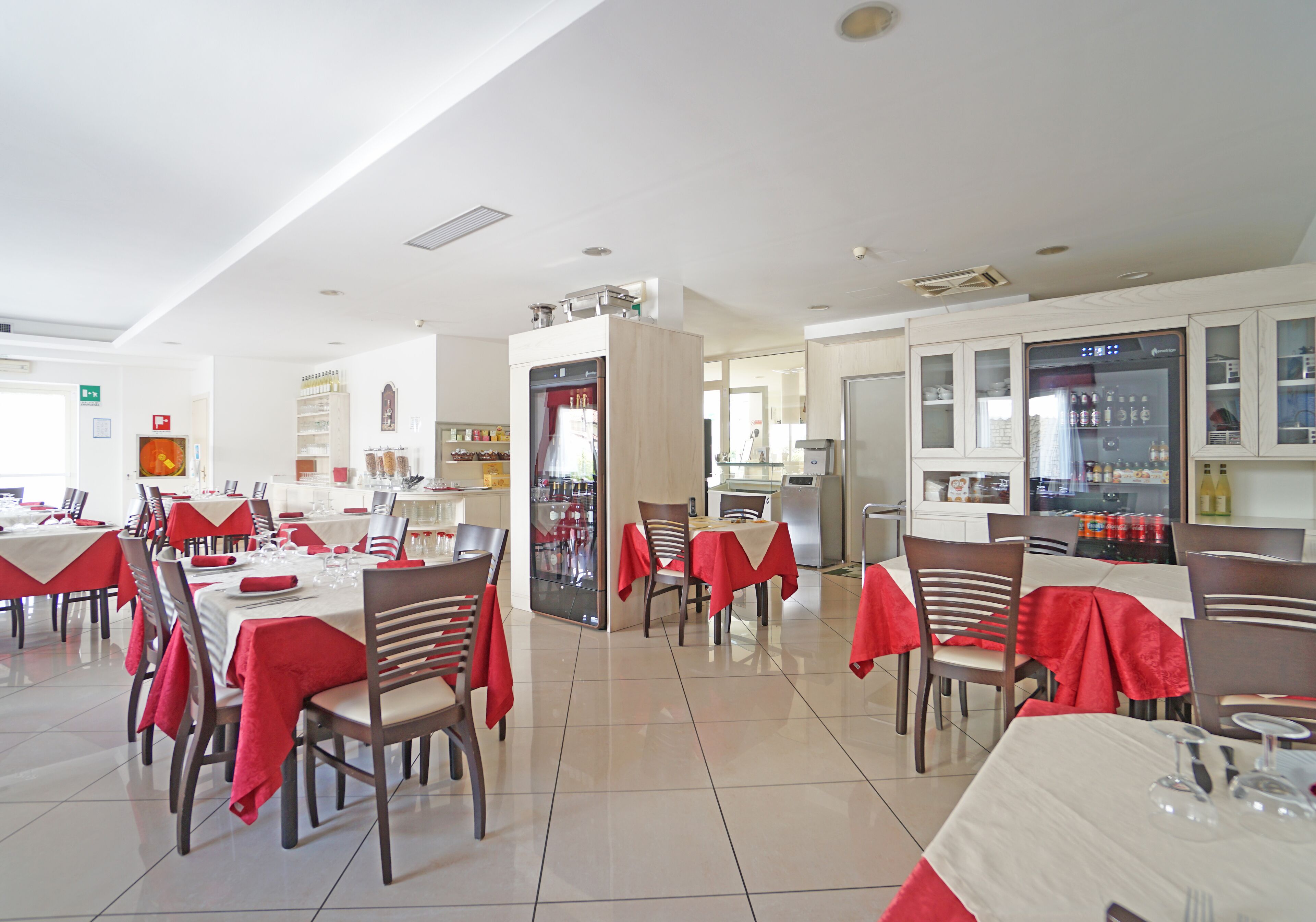 Un restaurant spacieux, doté de nombreuses tables et chaises, d’un espace cuisine et d’un réfrigérateur rempli de boissons.