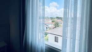 A window with sheer curtains, offering a view of a residential area with houses and trees. - Hotel Pigalle (Forte dei Marmi)