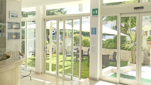 A hotel reception area with a glass door leading to an outdoor patio with chairs and a table. - Hotel Pigalle (Forte dei Marmi)