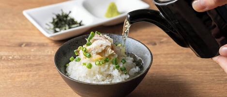 A bowl of rice with green onions and a piece of meat, being poured from a black pitcher.