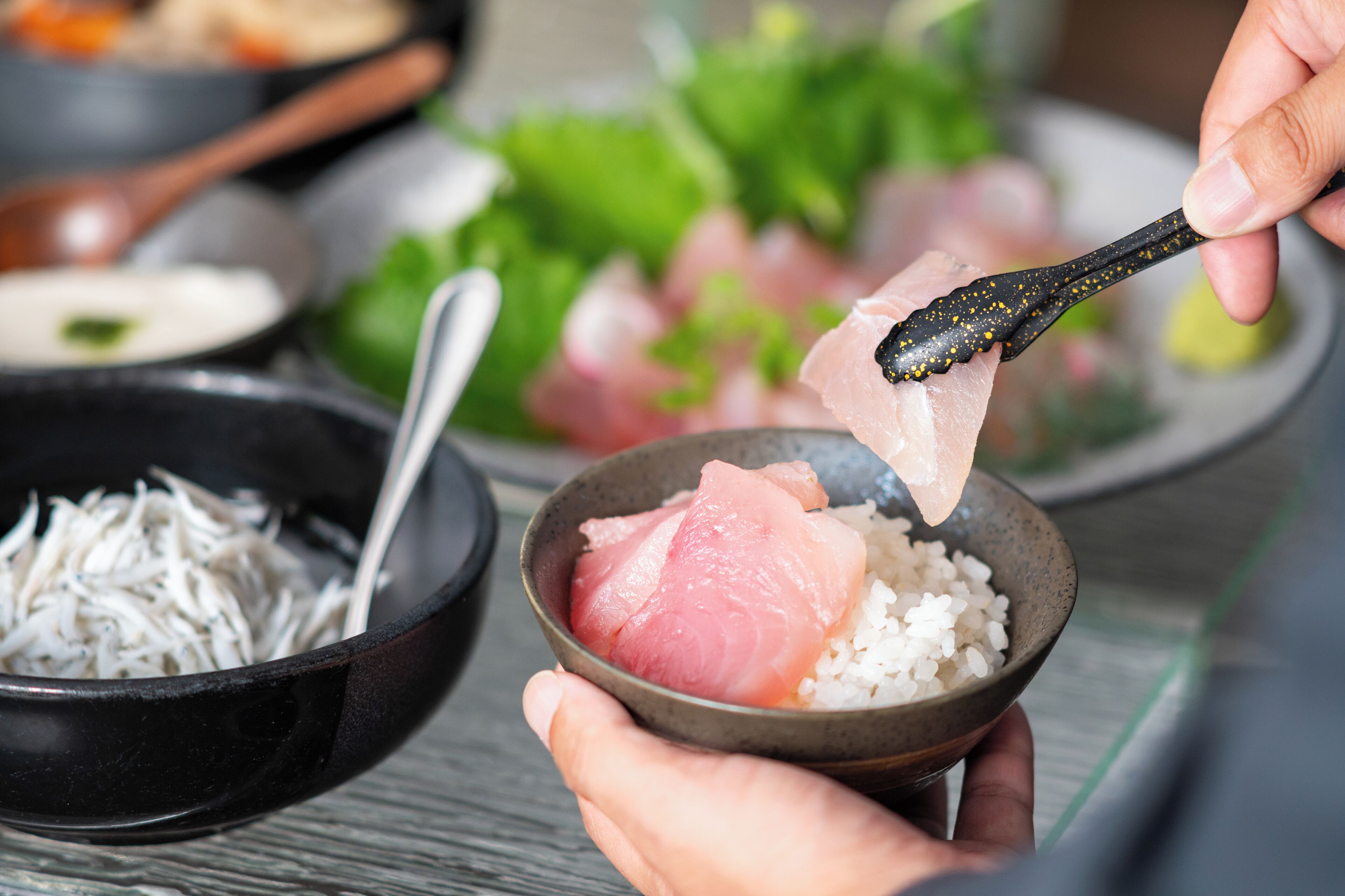A bowl of sashimi with rice, a spoon, and shredded daikon radish.