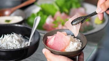 A bowl of sashimi with rice, a spoon, and shredded daikon radish.
