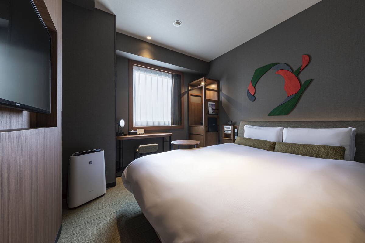 A hotel room with a large bed, a desk with a chair, a TV, and a window with curtains.