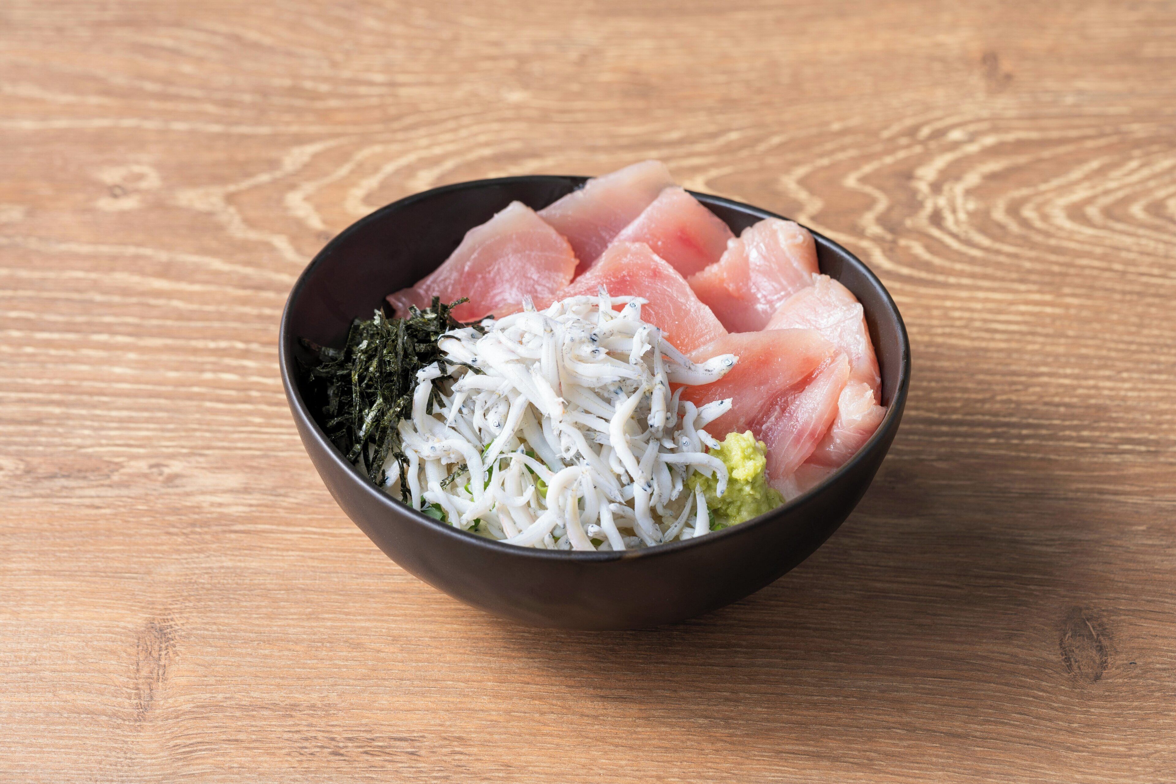 Un tazón de sashimi con algas y wasabi sobre una mesa de madera.