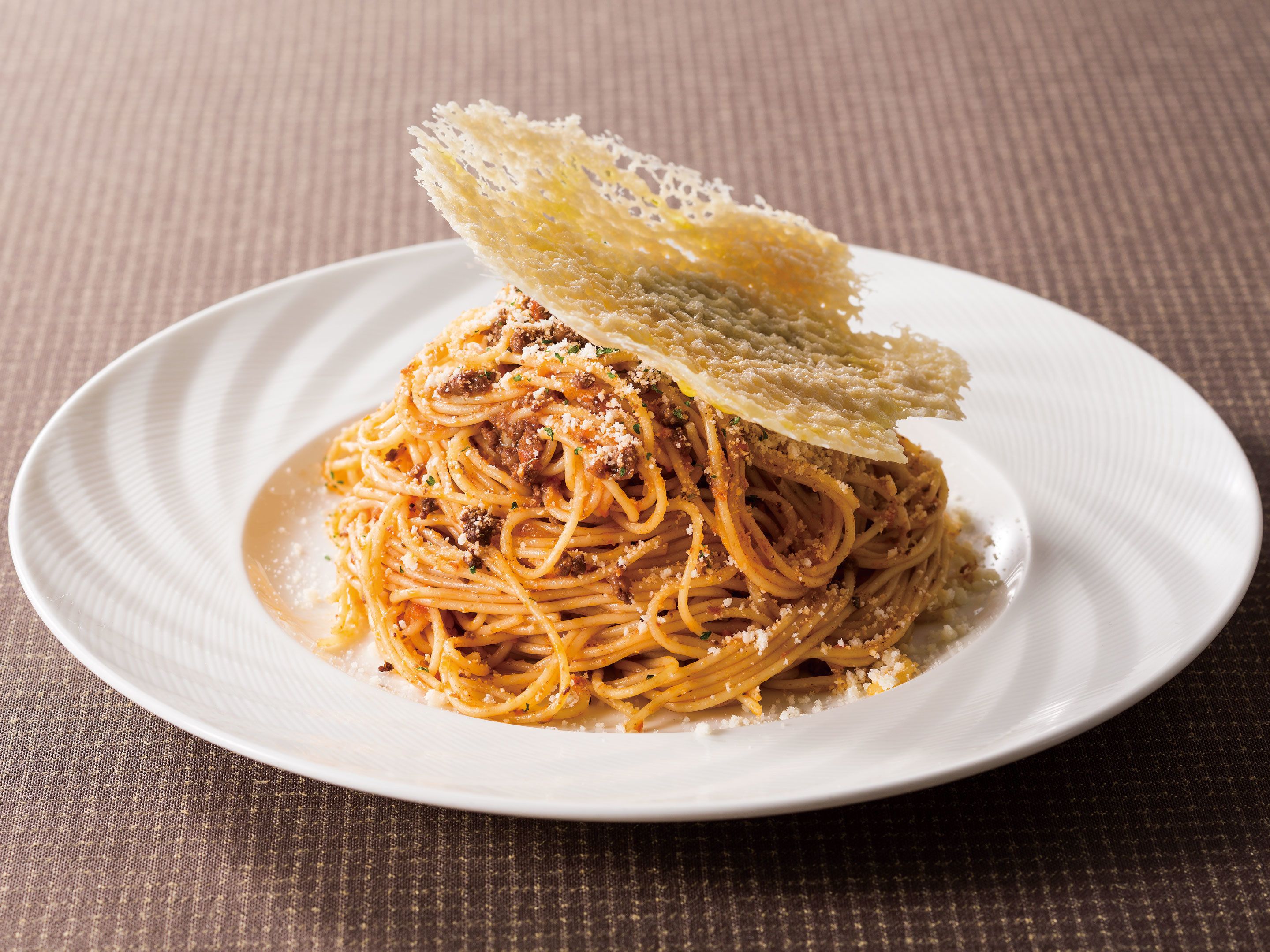 A plate of spaghetti with meat sauce and grated cheese, topped with a crispy wafer.