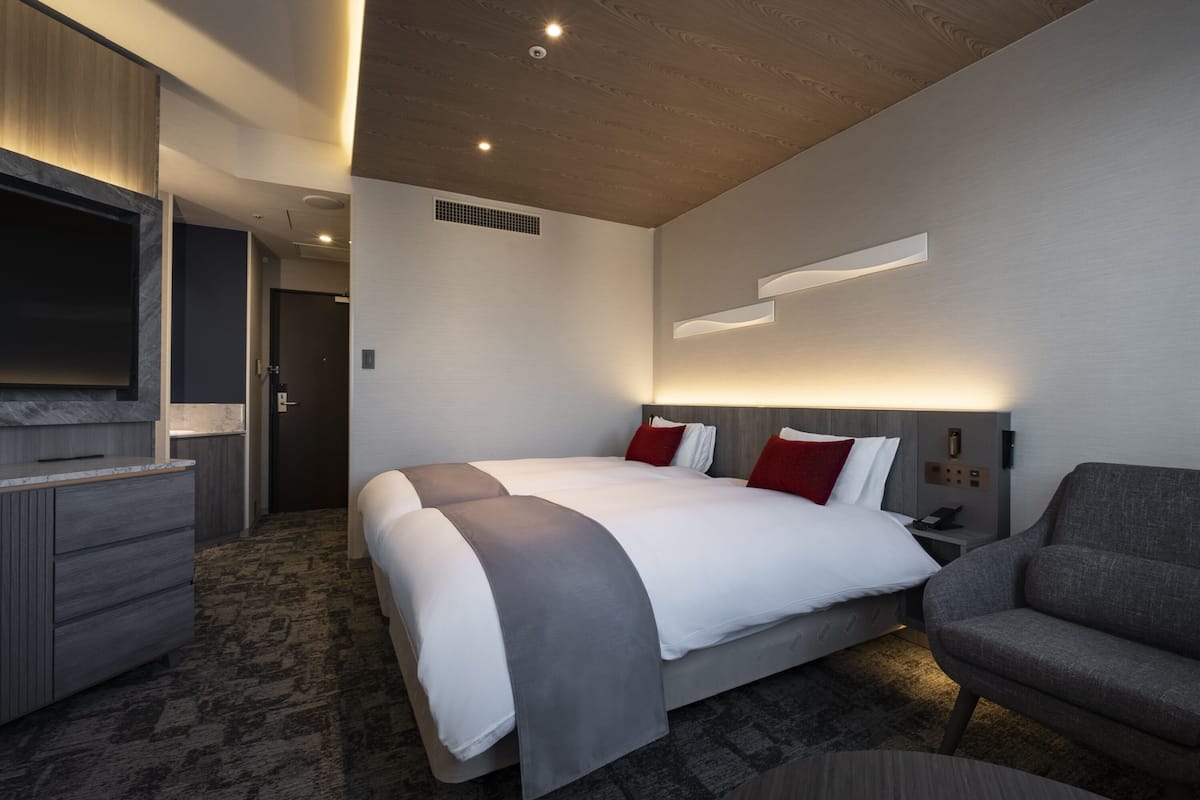 A modern hotel room with a large bed, a desk, a chair, and a TV.
