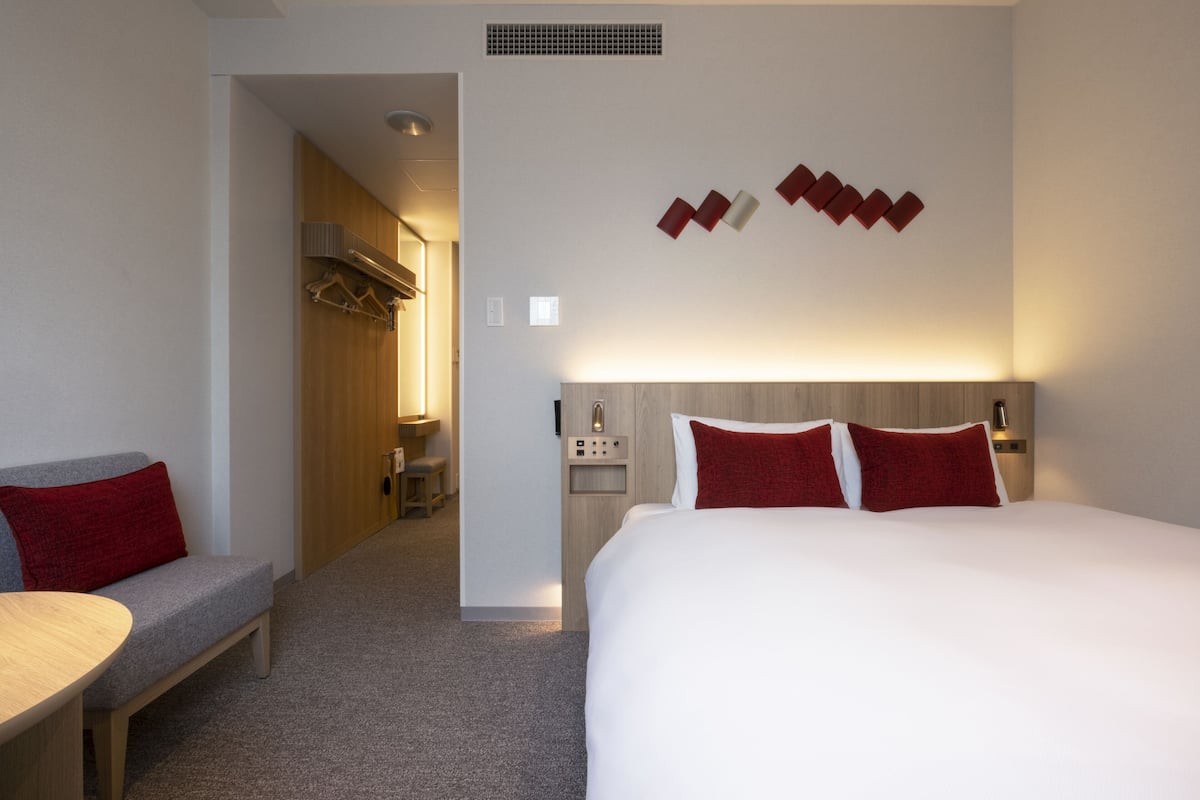A hotel room with a large bed, a bedside table, a bench, and a wardrobe.