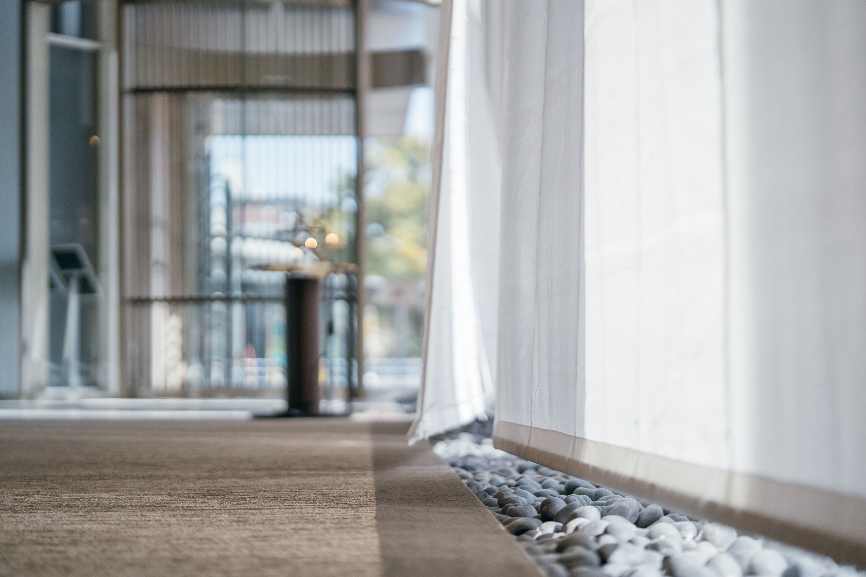 A corridor with a carpeted floor, a stone border, and a glass door leading to an outdoor area.