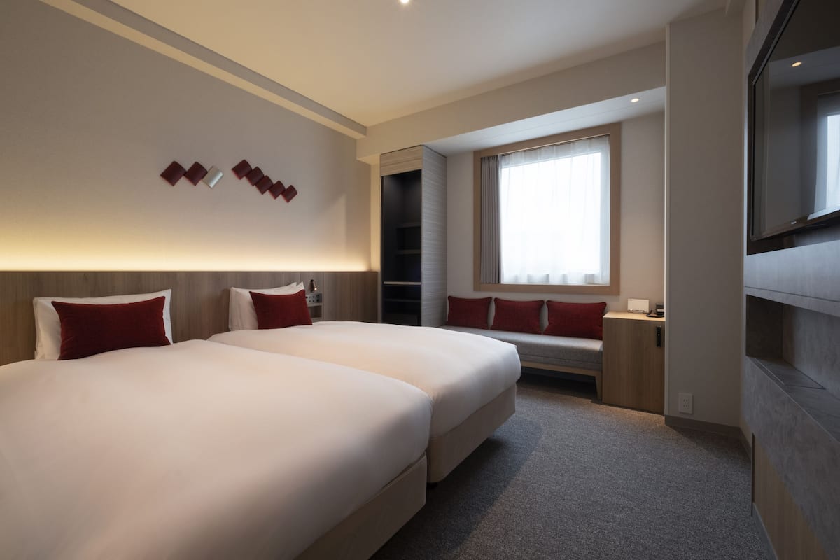 A modern hotel room with two large beds, a TV, and a large window.