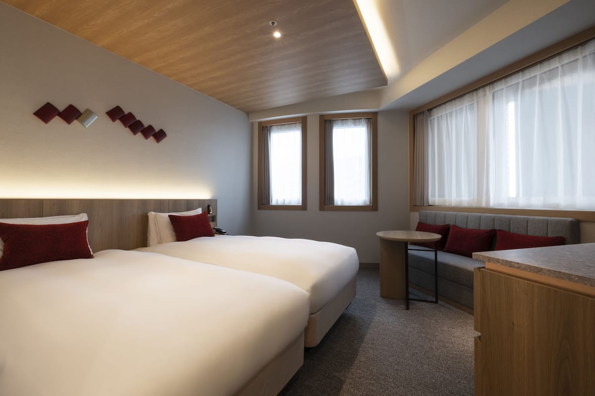 A hotel room with two beds, a small table, and a window with curtains.