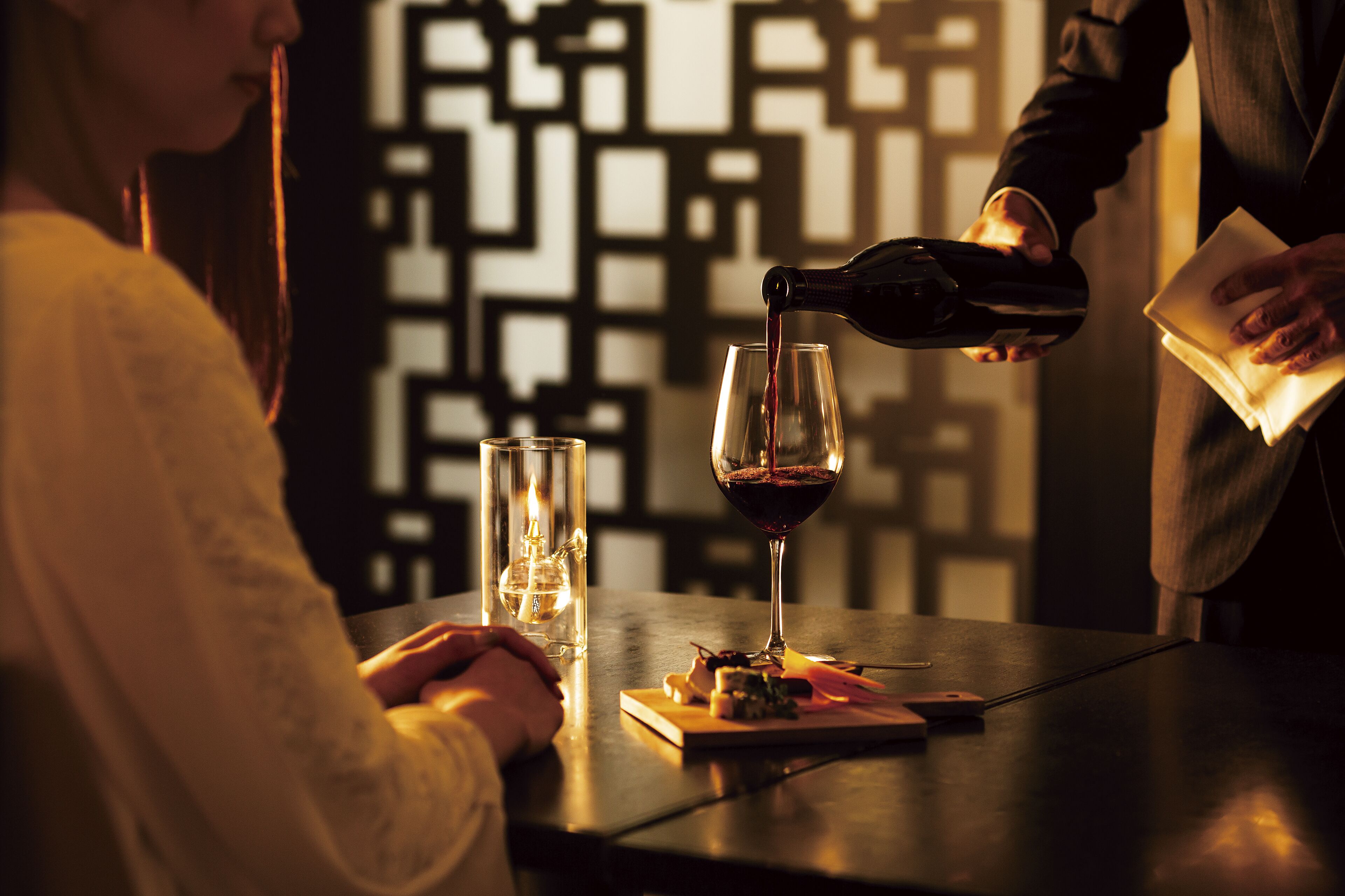 Una persona sirve vino en una copa sobre una mesa con una vela y un menú.