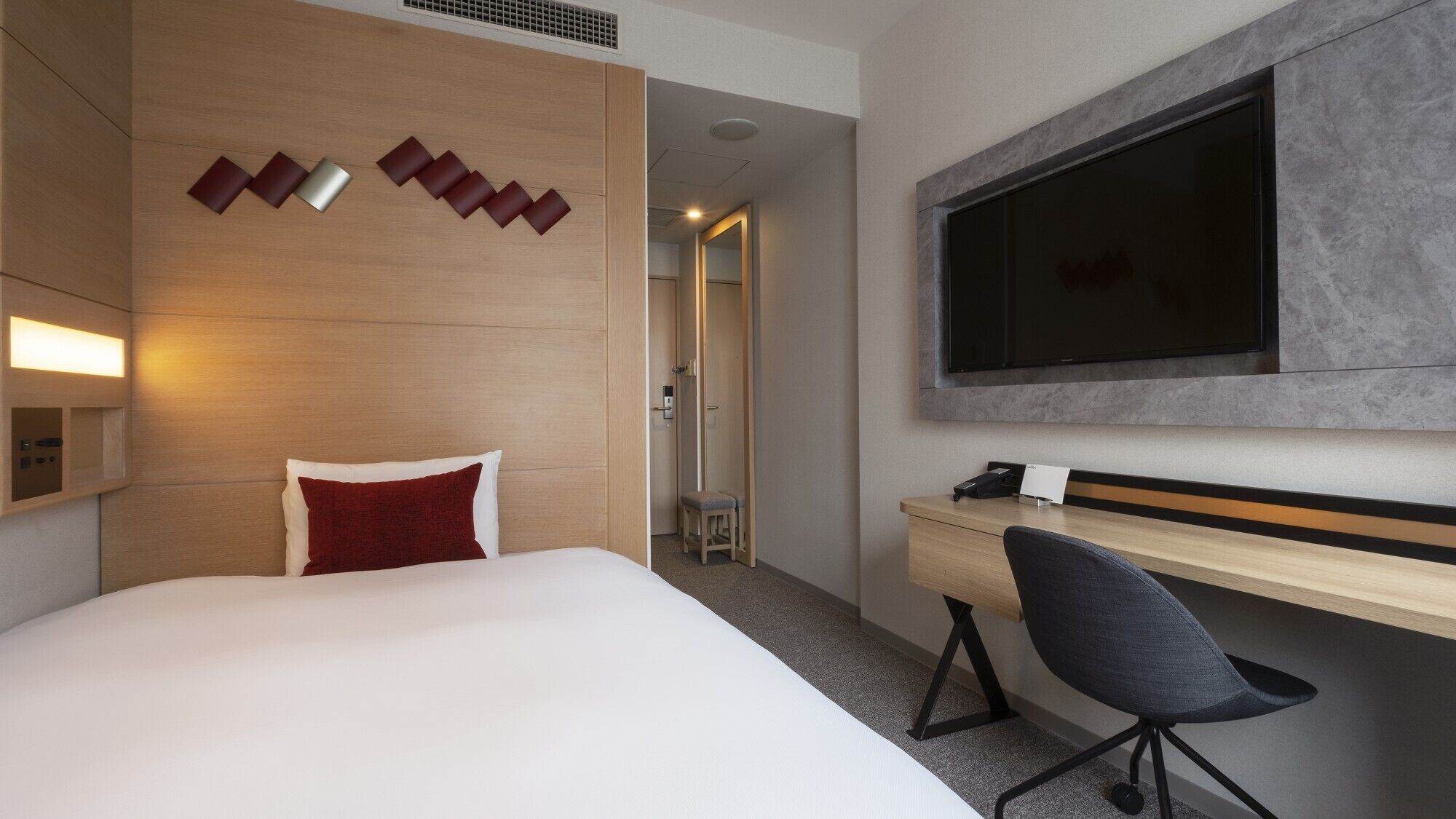 A hotel room with a bed, a desk, a chair, a TV, and a shower area.