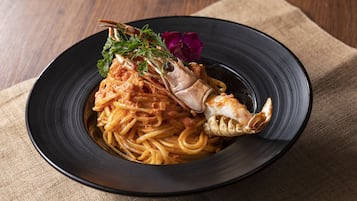A plate of spaghetti with a lobster tail and garnish on a black plate.