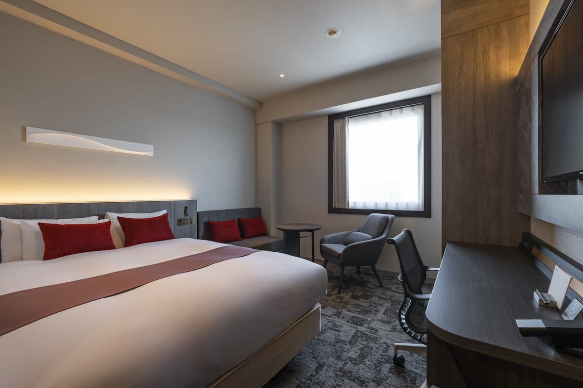 A hotel room with a large bed, a desk, a chair, and a window.