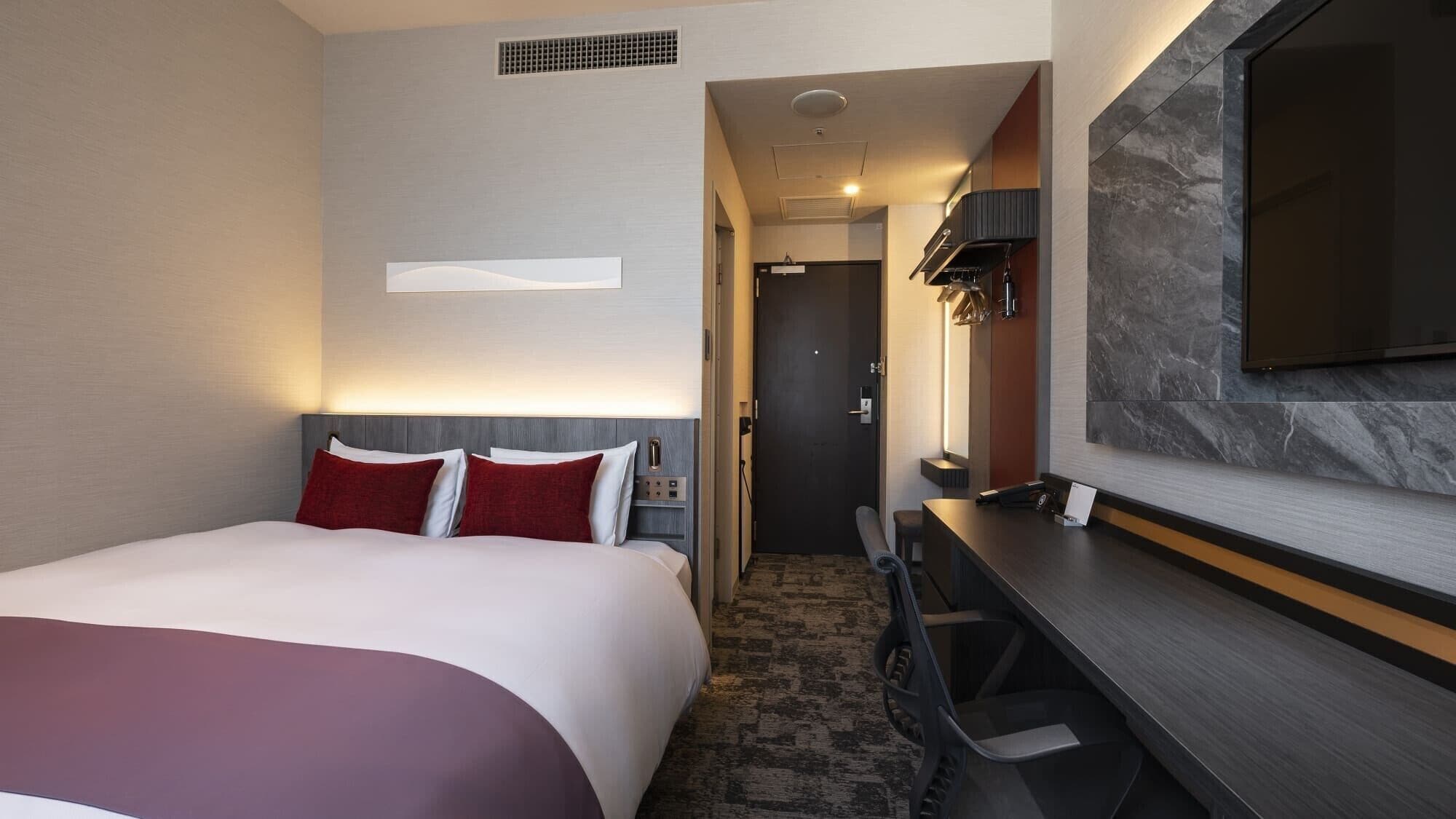 A hotel room with a bed, desk, and TV.