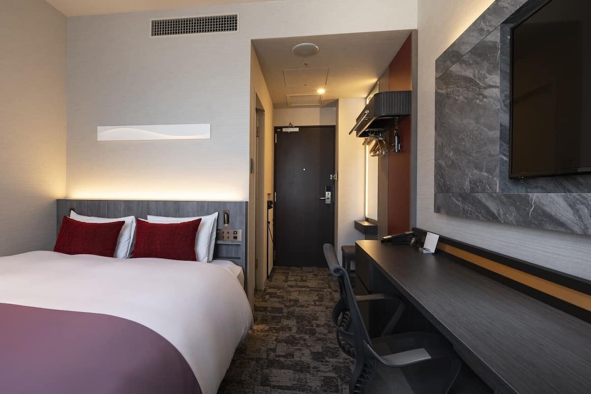 A hotel room with a bed, desk, and TV.