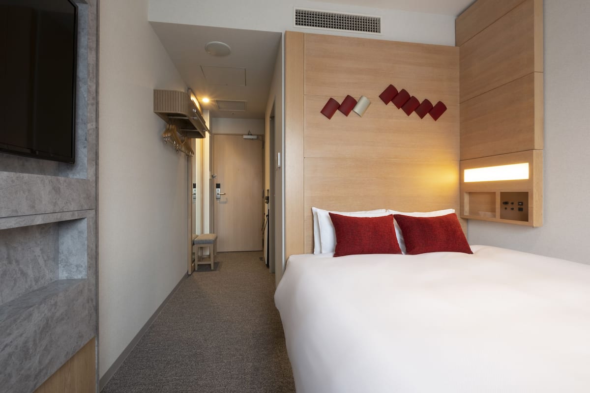 A hotel room with a large bed, a wooden headboard, a flat-screen TV mounted on the wall, and a small desk with a chair.