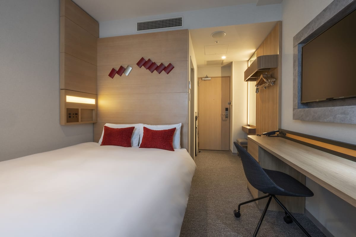 A hotel room with a bed, a desk, a chair, a TV, and a wardrobe.