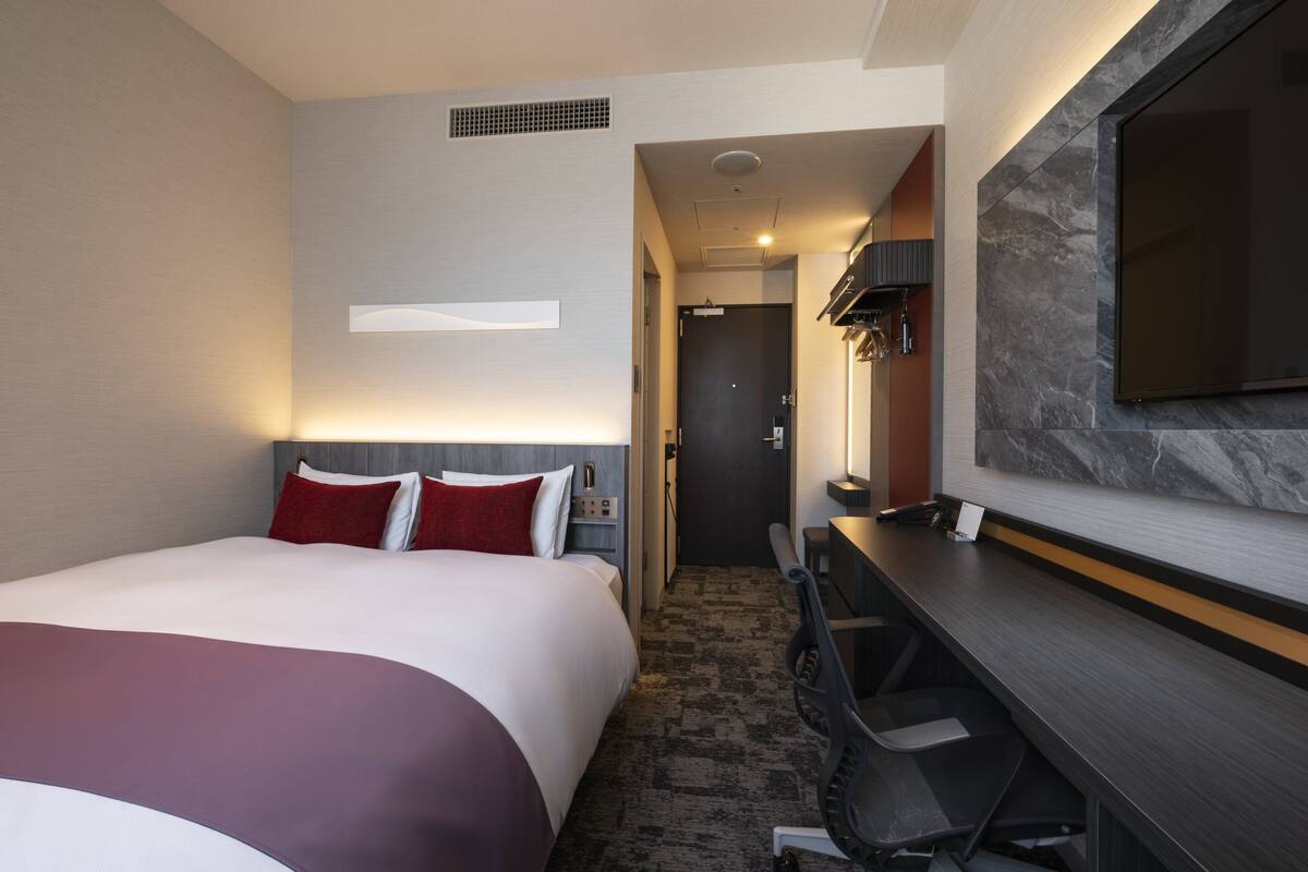 A hotel room with a large bed, a desk, and a TV mounted on the wall.
