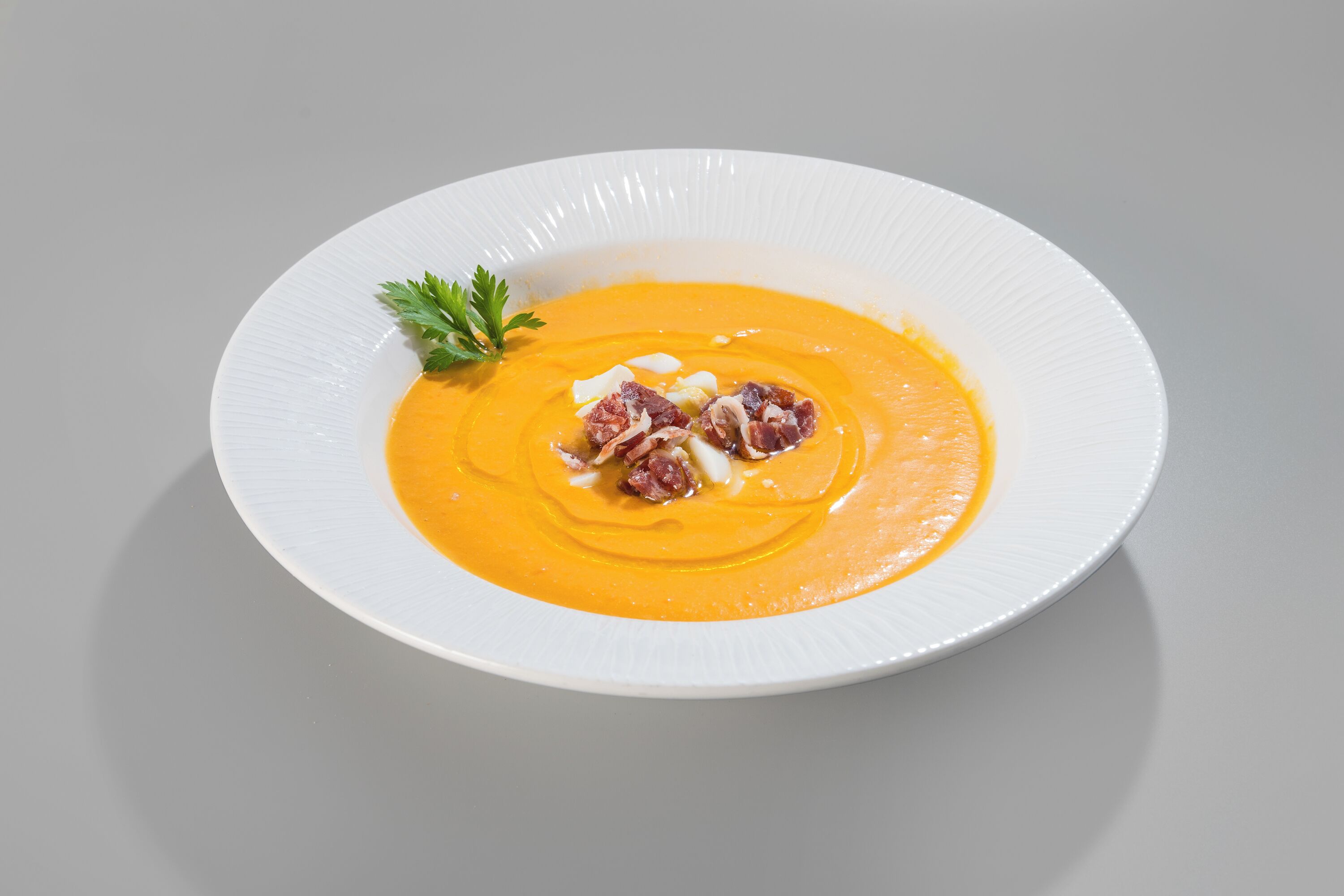 Un plato blanco con sopa cremosa anaranjada, adornado con tocino y perejil.