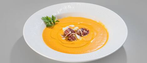 Un plato blanco con sopa cremosa anaranjada, adornado con tocino y perejil.
