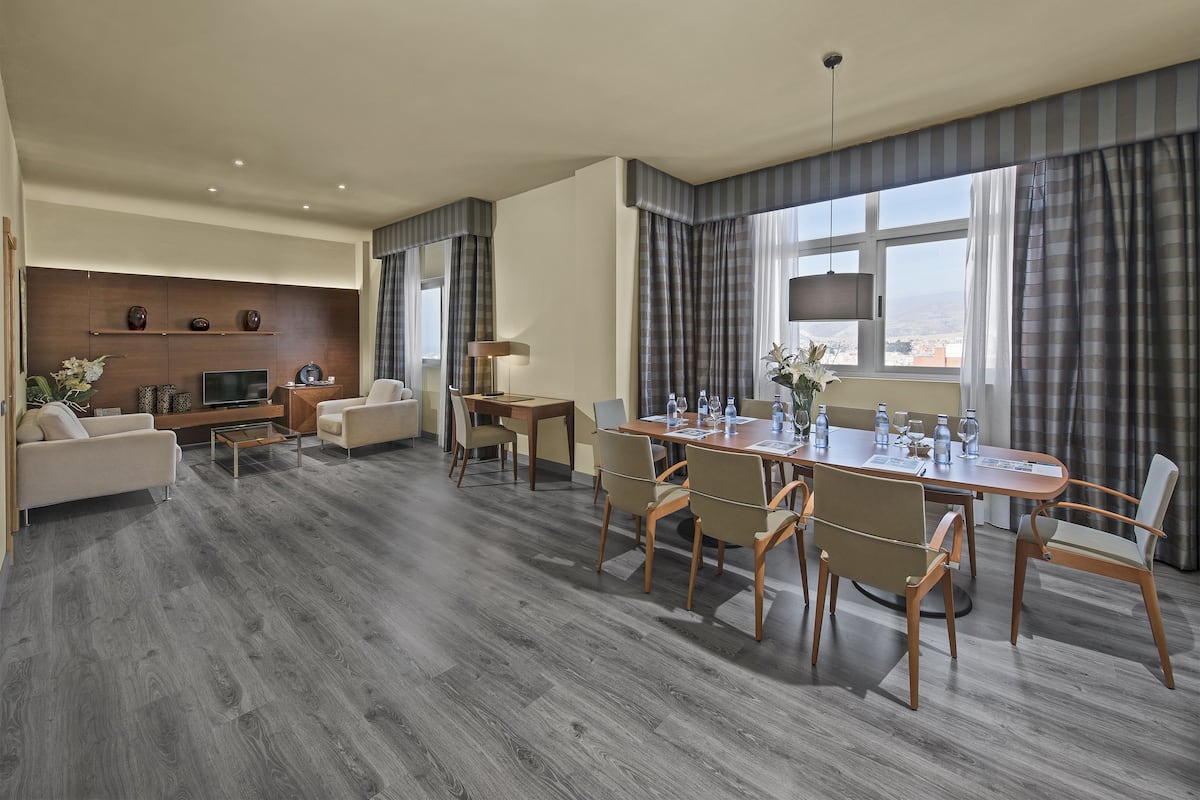 Een moderne hotelkamer met een zithoek, een zoutje, een televisie en een groot raam met gordijnen.