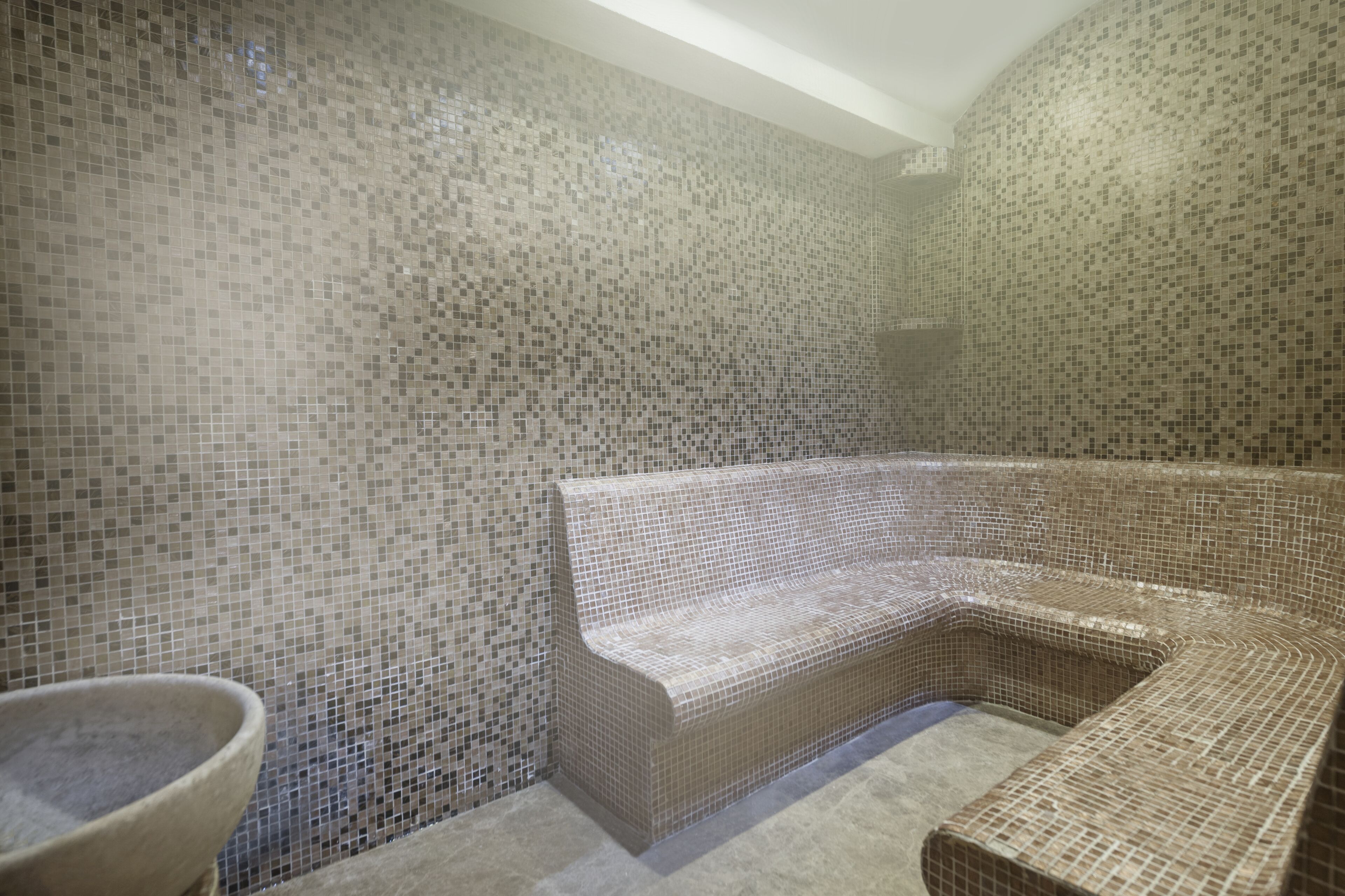 Un baño con paredes de mosaicos, una bañera independiente y un lavabo de piedra.