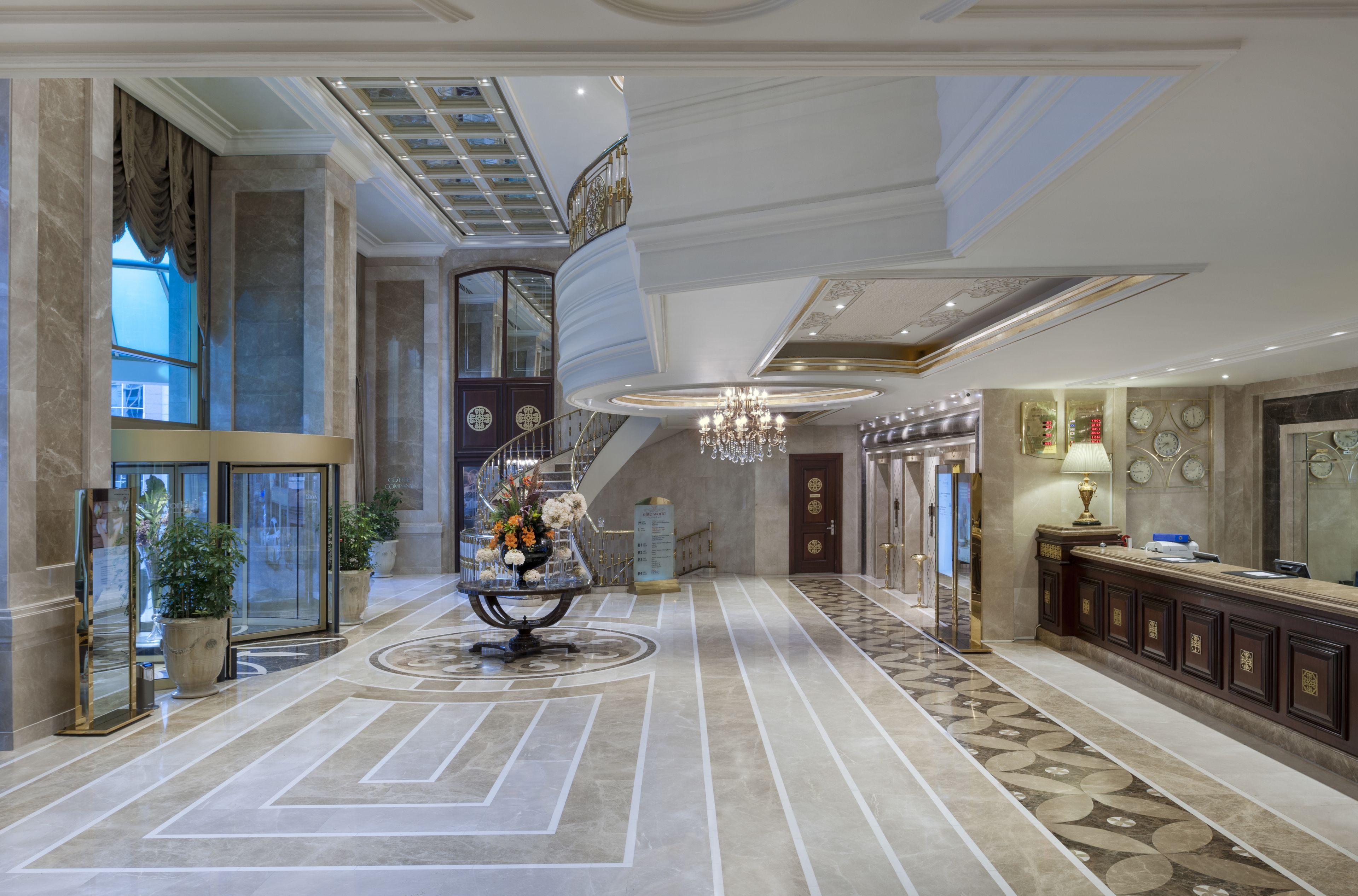A spacious lobby with a grand staircase, a chandelier, and a reception desk.