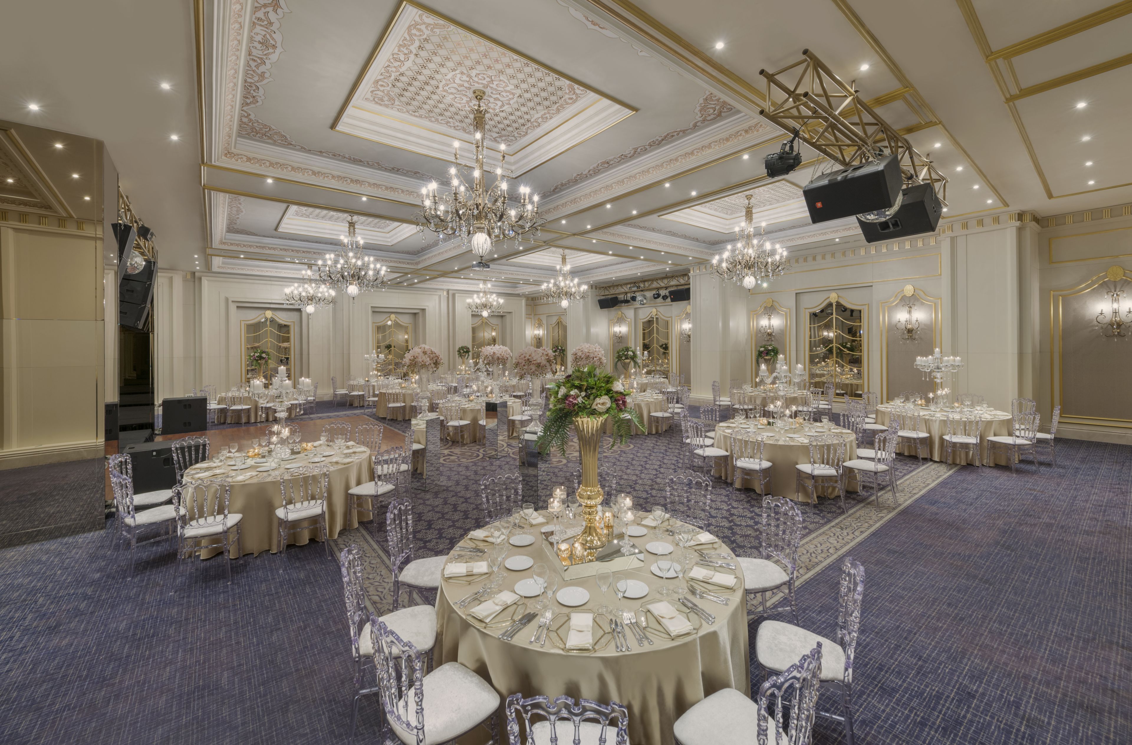 A banquet hall with round tables, chandeliers, and a stage.