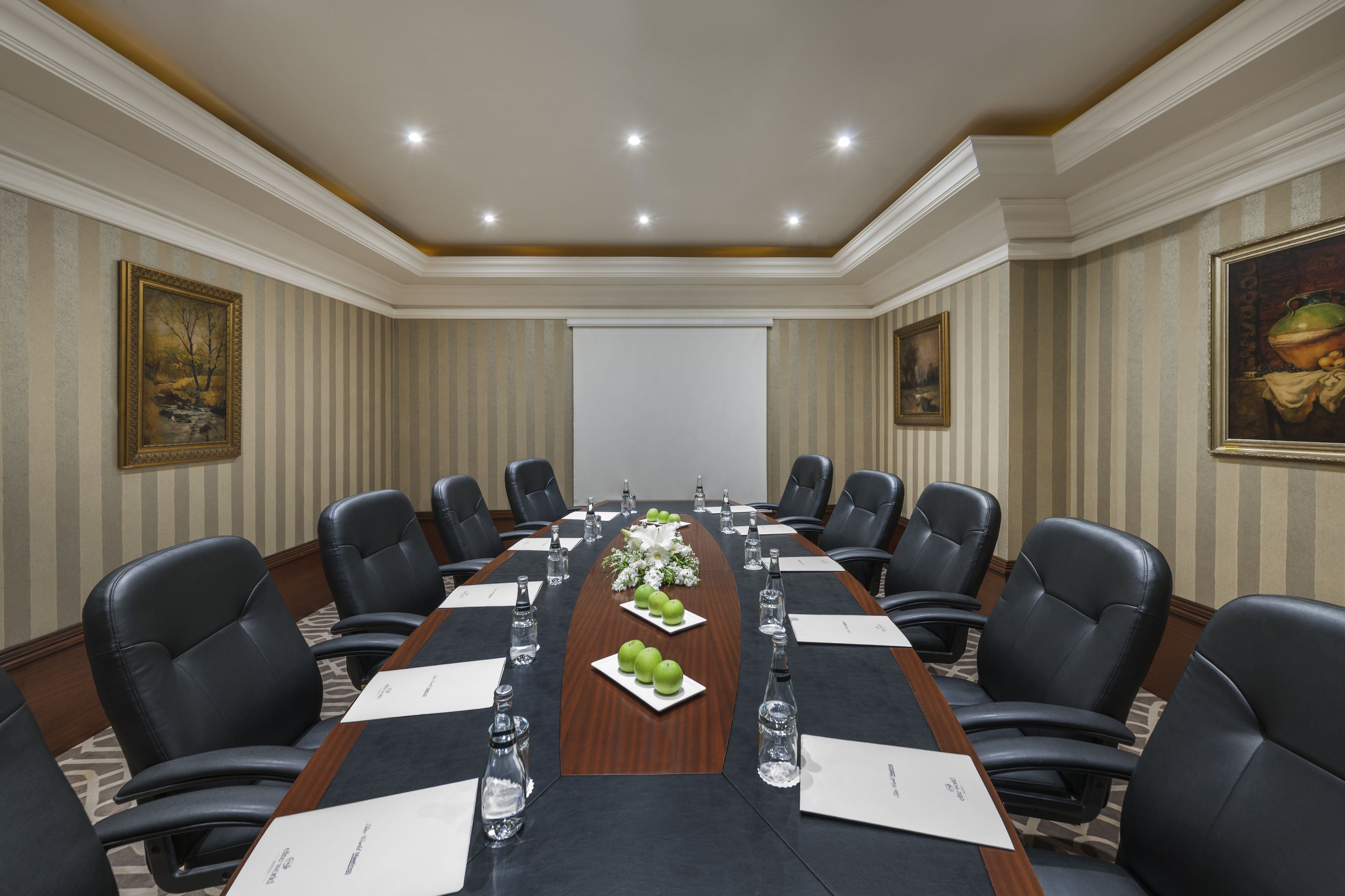 A conference room with a long table, black leather chairs, and a projector screen at the front.