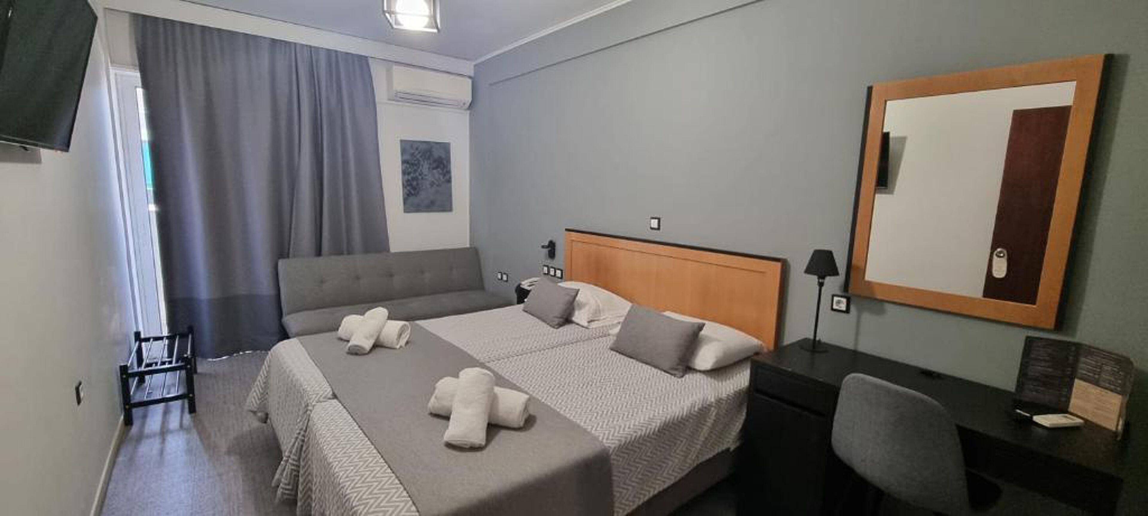 A hotel room with a bed, a desk, a chair, a mirror, and a window with curtains.