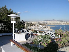 Un paisaje urbano costero con un puerto deportivo, un farol blanco y ruedas decorativas.