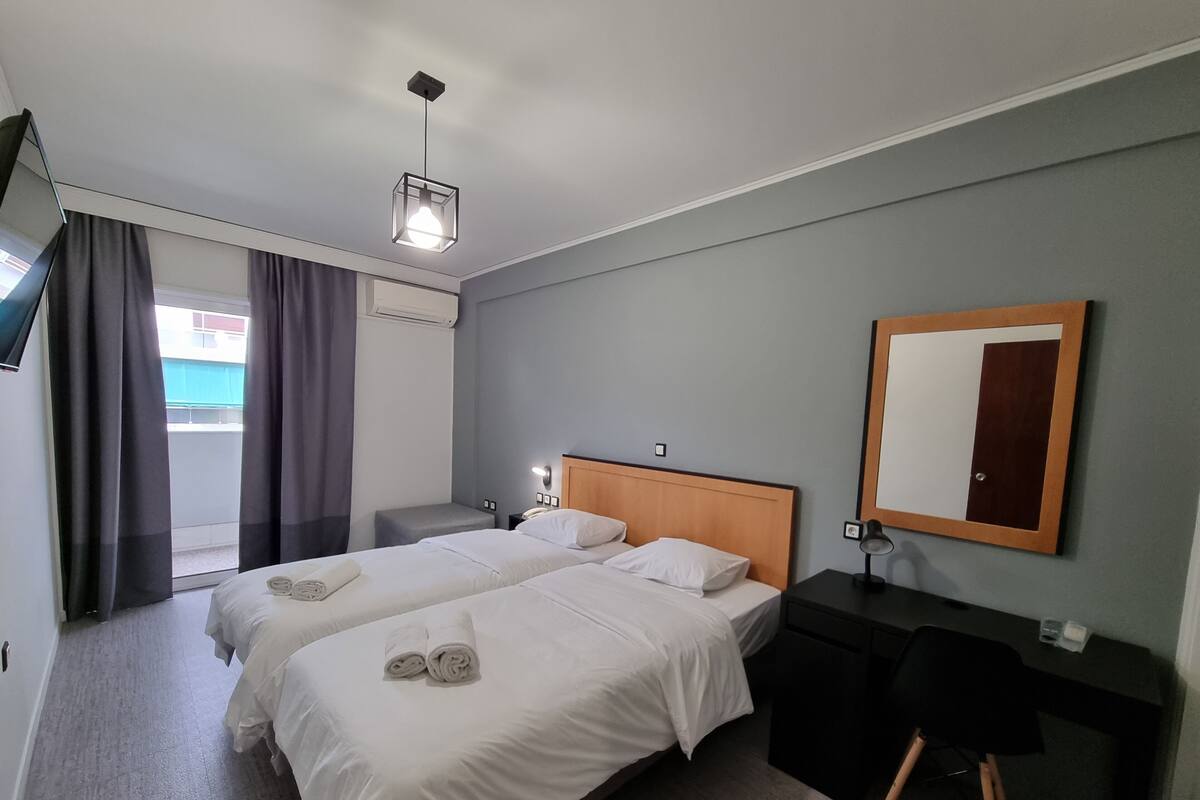 Habitación de hotel con dos camas, un escritorio, una silla, un espejo y una lámpara en el techo.