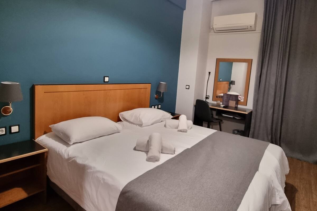 Una habitación de hotel con cama, escritorio, silla, espejo y aire acondicionado.