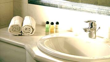 A bathroom with a sink, two rolled towels, and two bottles of toiletries.