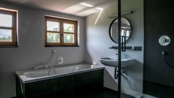 Ein modernes Badezimmer mit Badewanne, Waschbecken und Dusche. Fenster sorgen für natürliches Licht und Blick auf Bäume.