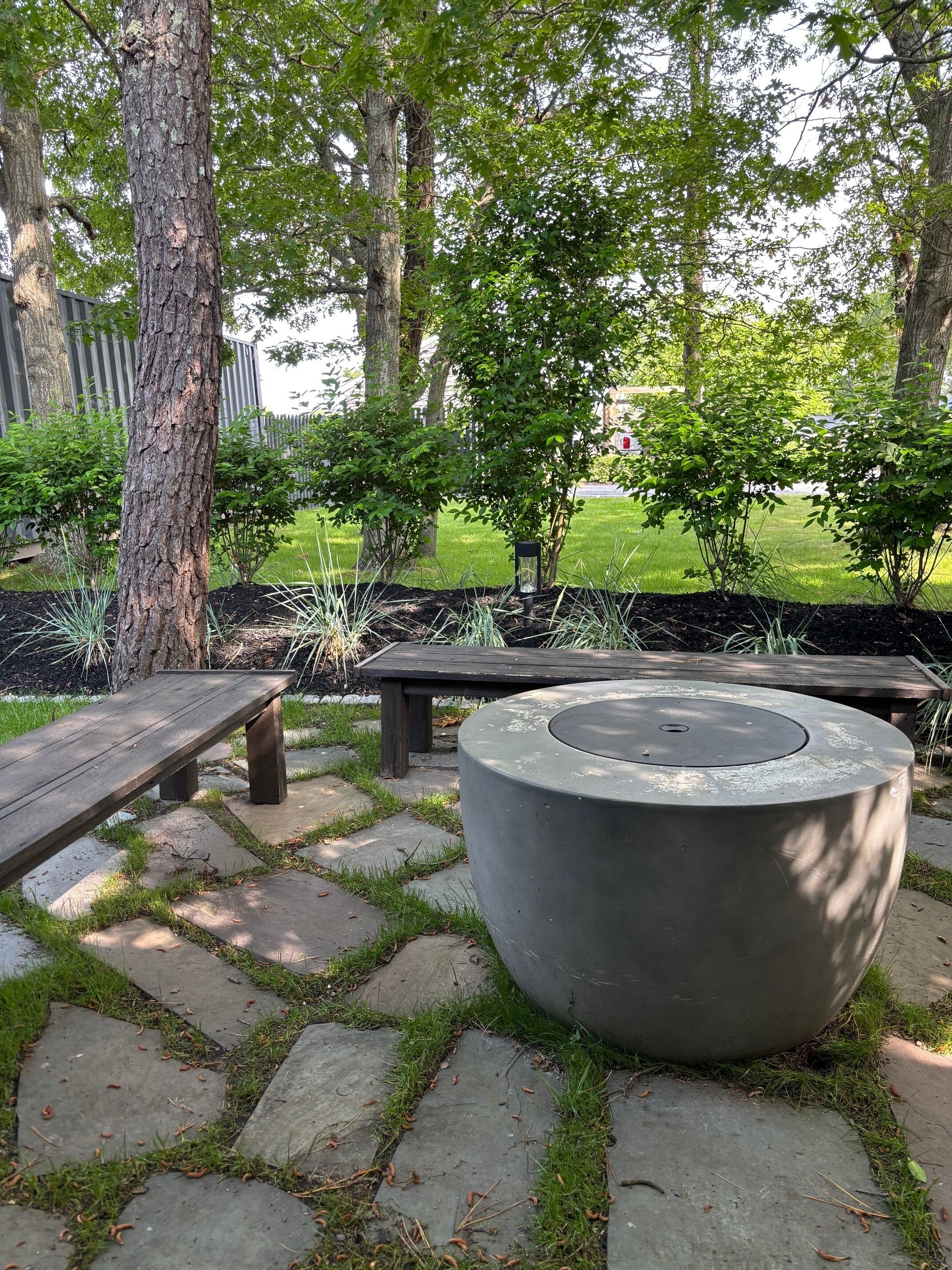 Un parc amb un camí de pedra, seients de fusta, una jardineria de formigó i arbres.