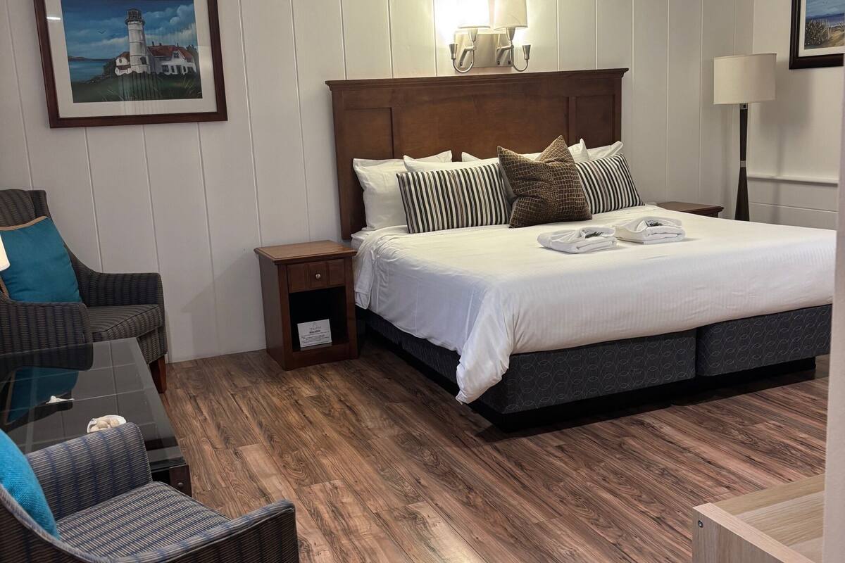 Una habitación de hotel con una cama grande, una mesita de noche, una silla y un cuadro de un faro en la pared.
