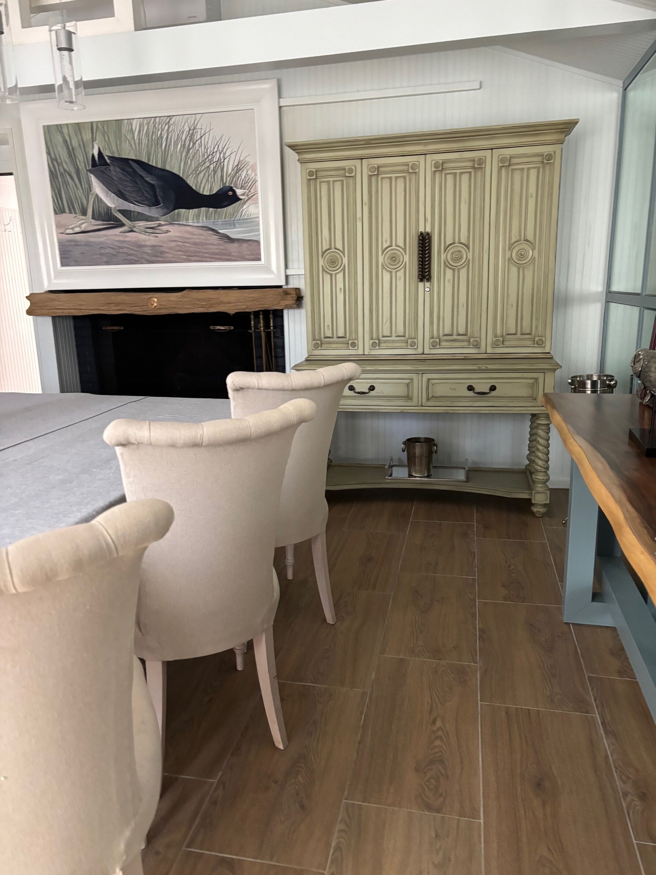 A dining area with a table and chairs, a cabinet with doors, and a painting on the wall.