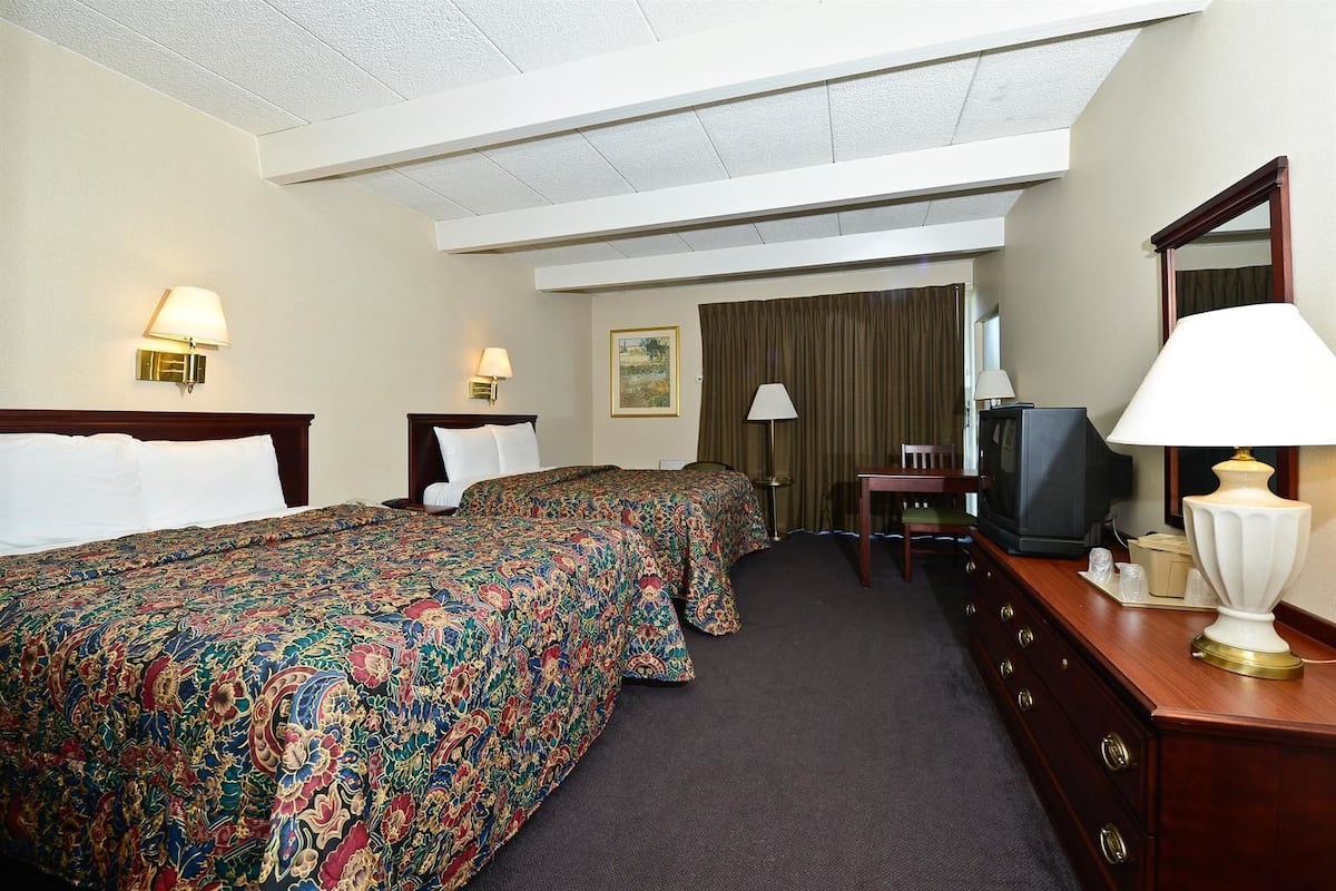 A hotel room with two beds, a desk, a television, and a mirror.