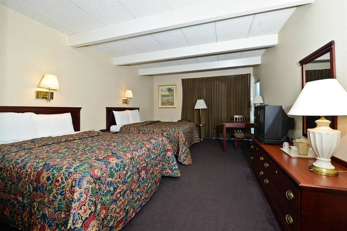 A hotel room with two beds, a desk, a television, and a mirror.
