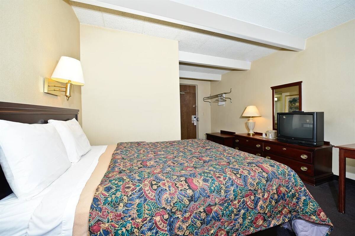 A hotel room with a bed, a television, a dresser, and a mirror.