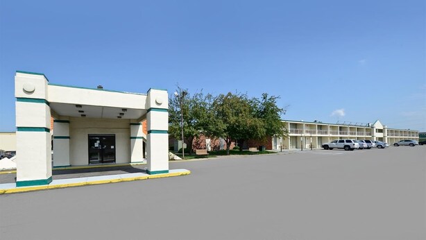A motel with a simple entrance, a parking lot, and a row of parked cars. - Americas Best Value Inn Phillipsburg (Phillipsburg)