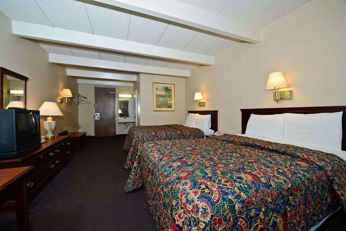 A hotel room with two beds, a television, a desk, and a bathroom.