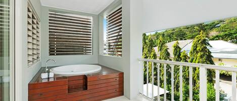 Un balcón con vistas a una zona residencial, una bañera de madera y una ventana con persianas.