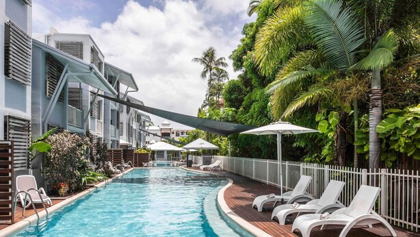 A swimming pool with lounge chairs and umbrellas, surrounded by greenery and a white fence. - Mantra Aqueous on Port (Port Douglas)