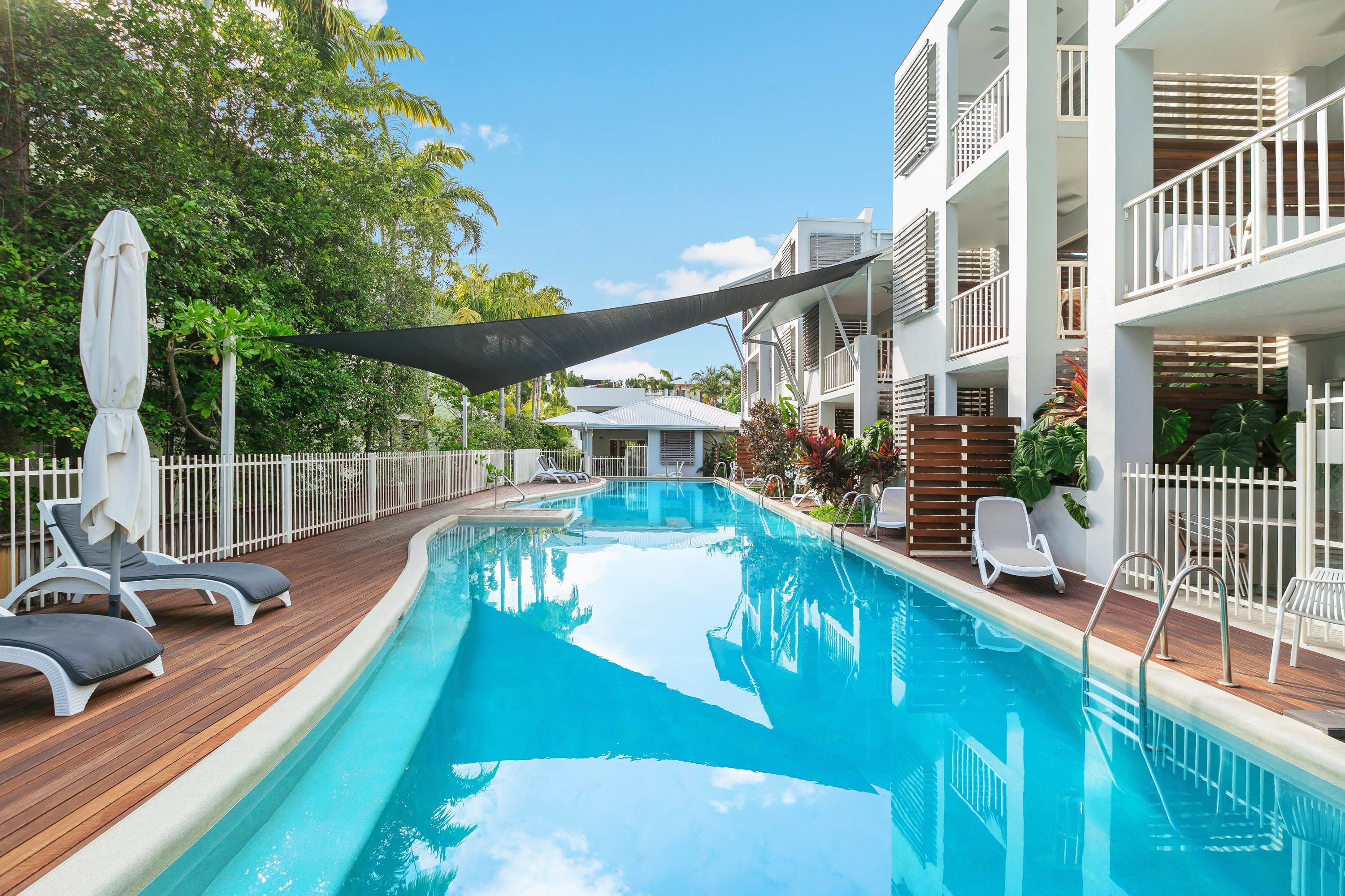 A swimming pool with lounge chairs, a shaded area, and a building with balconies.