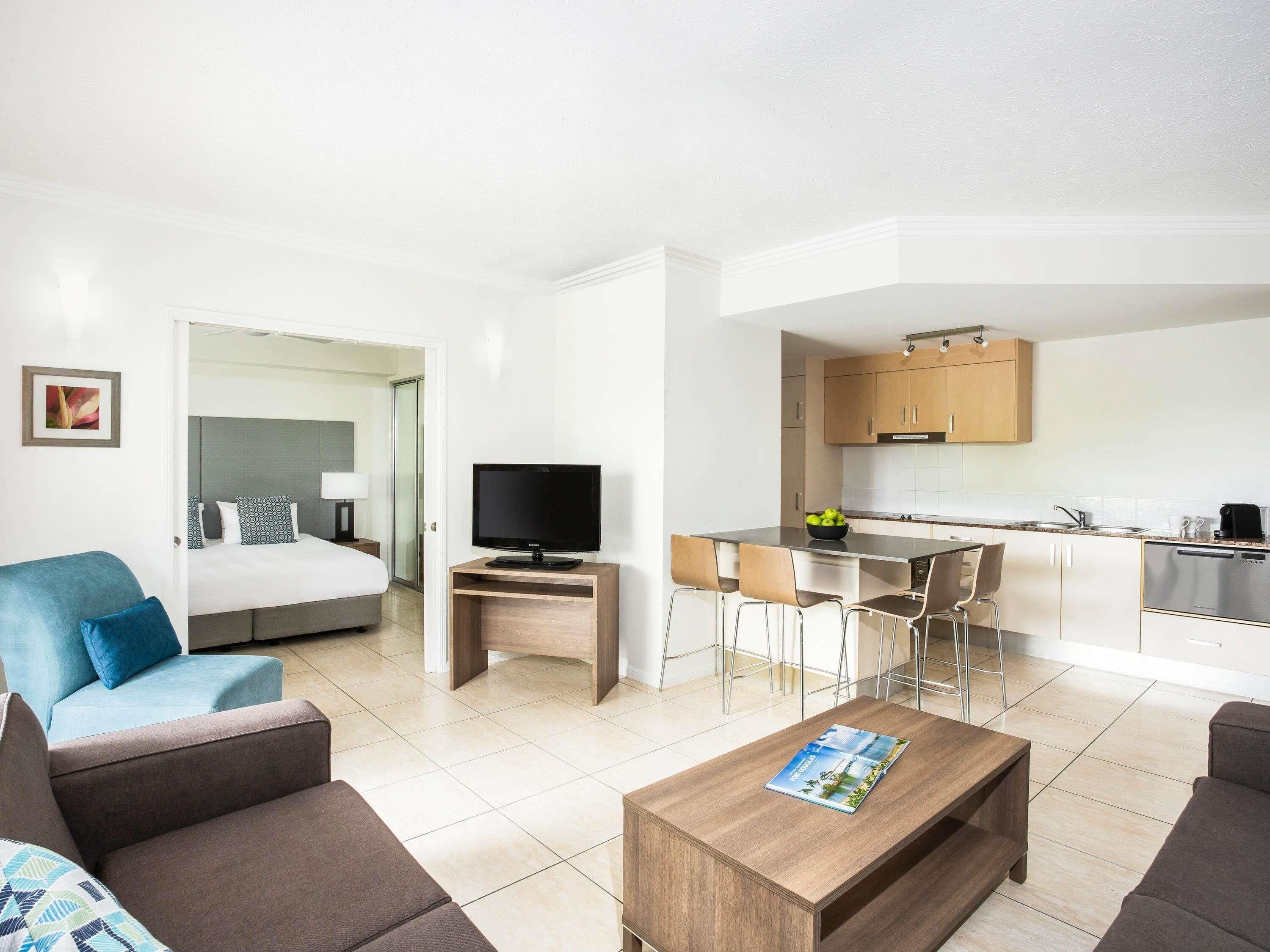 Una habitación de hotel moderna con cama, televisor, zona de comedor y cocina.