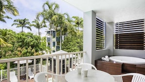 A balcony with a pool, white chairs, a table, and a hot tub. - Mantra Aqueous on Port (Port Douglas)