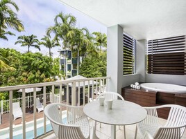 A balcony with a pool, white chairs, a table, and a hot tub.